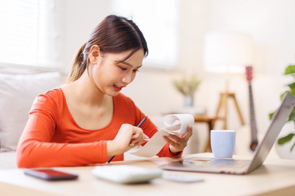 หญิงสาวกำลังคำนวณค่าใช้จ่ายบ้านที่ยังผ่อนอยู่ สำหรับขอกู้ต่อเติม รีโนเวทบ้าน