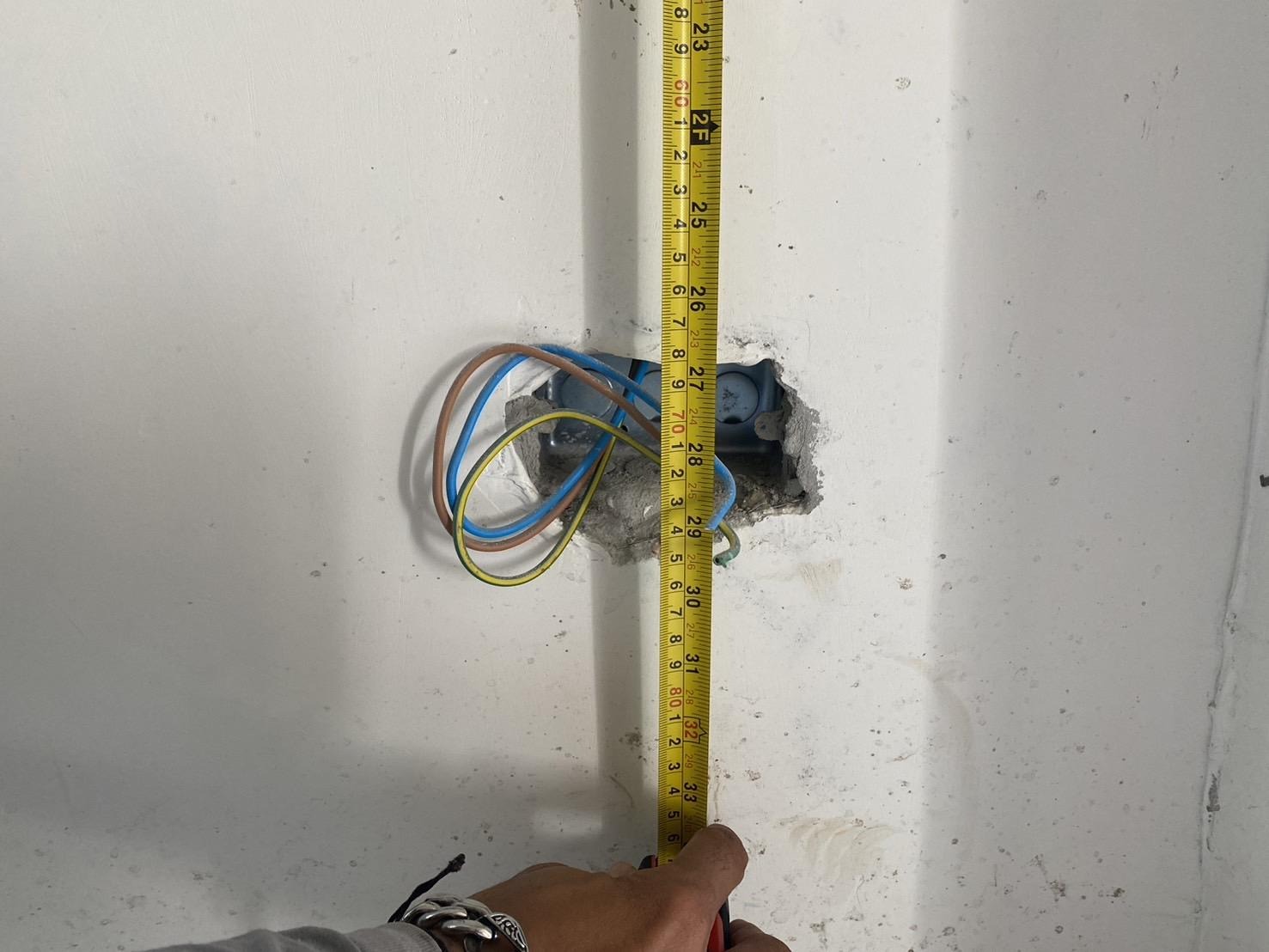 04_ap-house-electrical-system.jpg ช่างกำลังใช้ตลับเมตรวัดระดับความสูงของการติดตั้งกล่องสายไฟบนผนังให้ได้ตามมาตรฐาน
