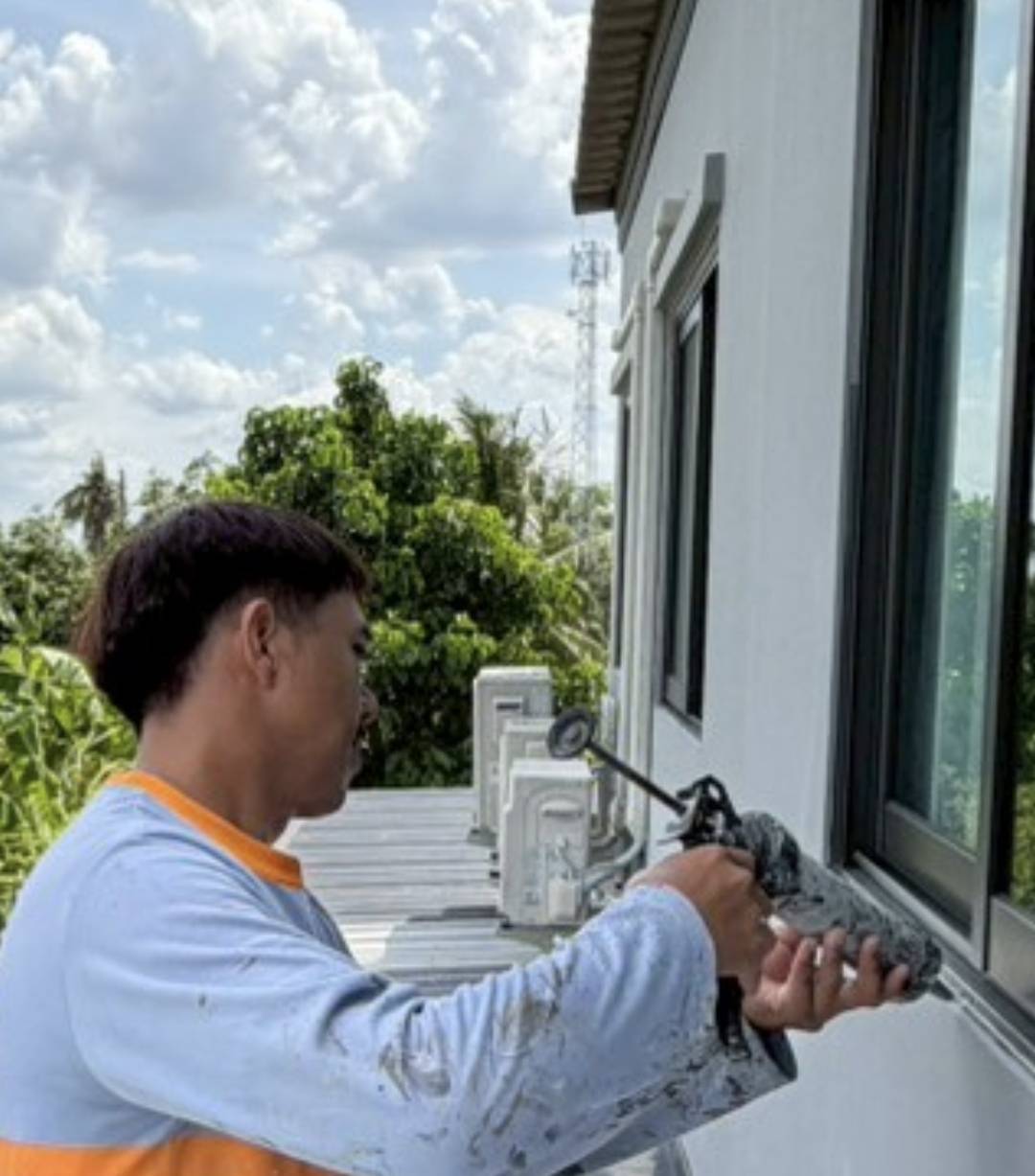 ช่างของ AP กำลังใช้เครื่องมือขูดลอกวัสดุเดิมและยิงซิลิโคนอุดรอยต่อรอบกรอบหน้าต่างใหม่