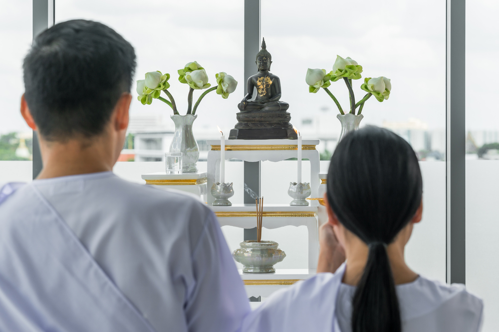 ผู้ชายและผู้หญิงกำลังกราบไหว้พระพุทธรูปที่วางอยู่บนหิ้งพระ